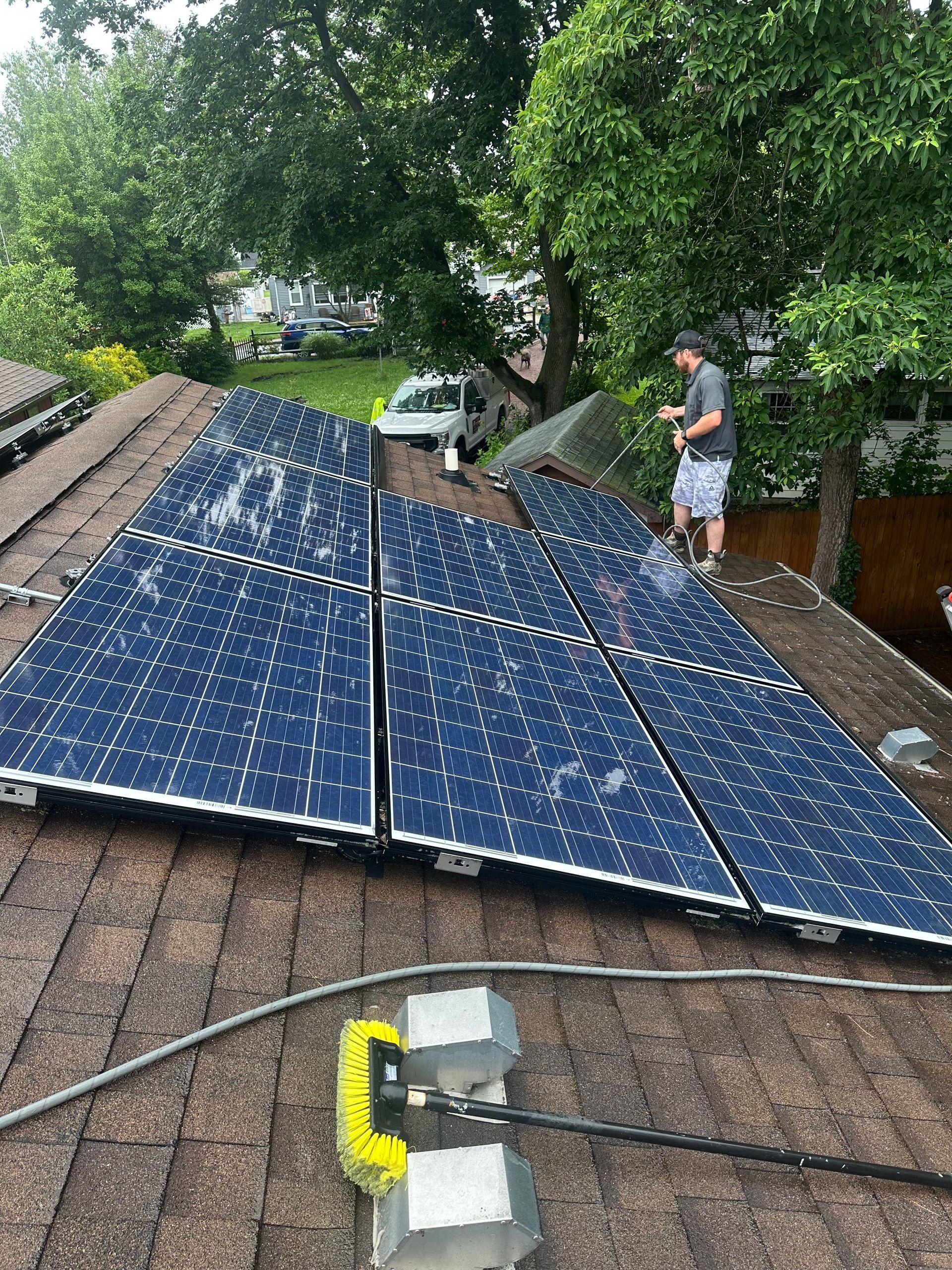 Solar panels on a sloped roof beside trees, with a person inspecting them.