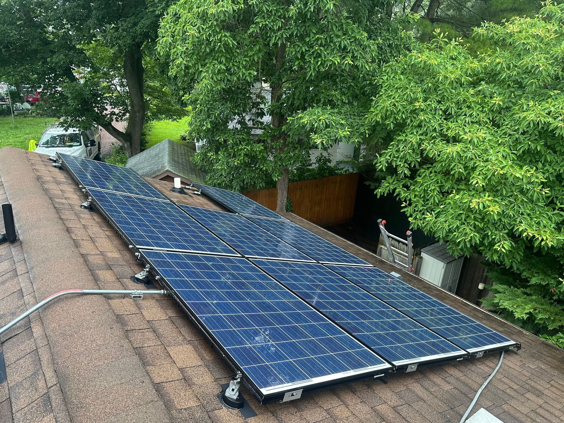 Blue solar panels installed on a sloped roof beside trees and a house