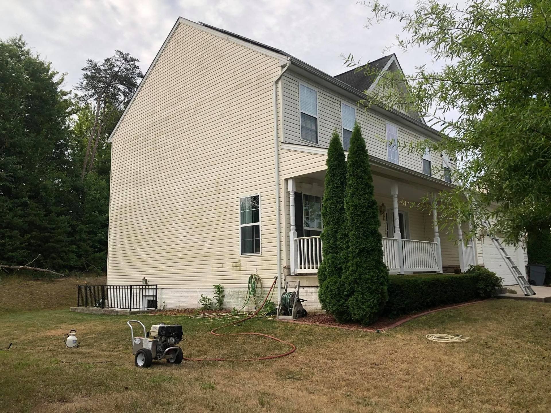 White two-story house with porch, tall shrubs, and a lawn mower on the front yard