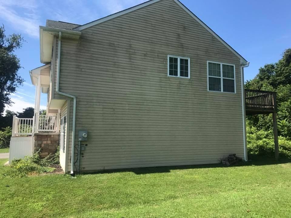 Side view of a beige house with white trim, small porch, and green lawn under a blue sky