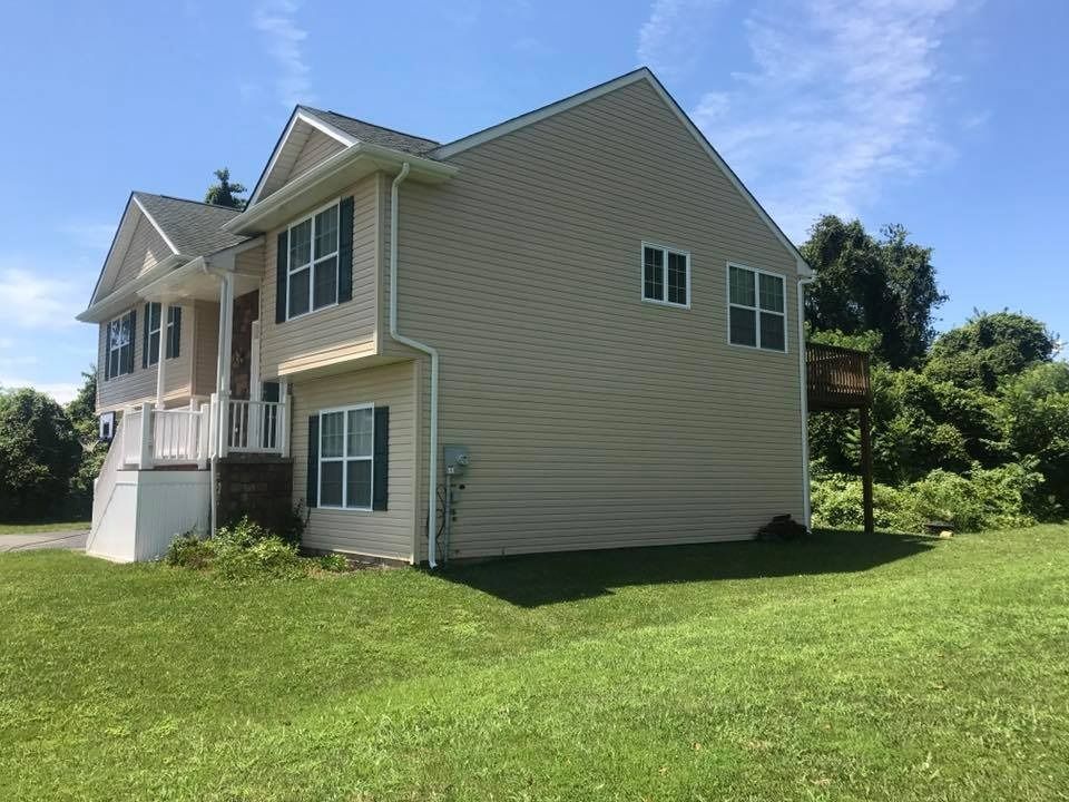 Beige two-story house with white trim on a green lawn under a blue sky