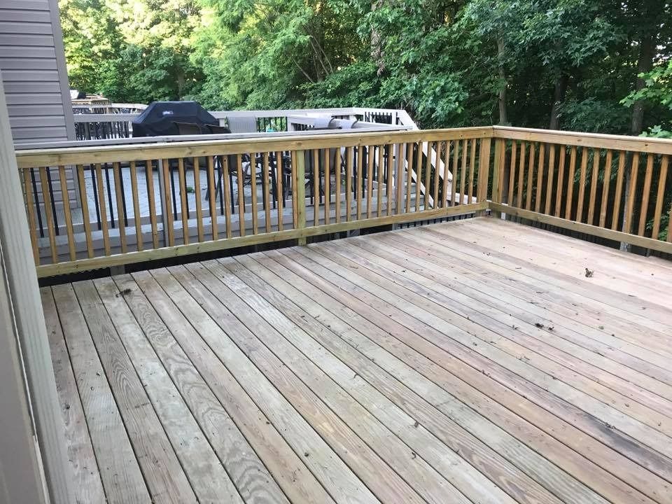 Empty wooden deck with railing overlooking trees and a parked truck.