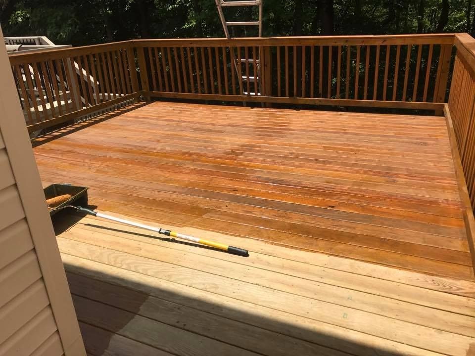 Wooden backyard deck with railings, showing a freshly stained section next to an unfinished lighter area.
