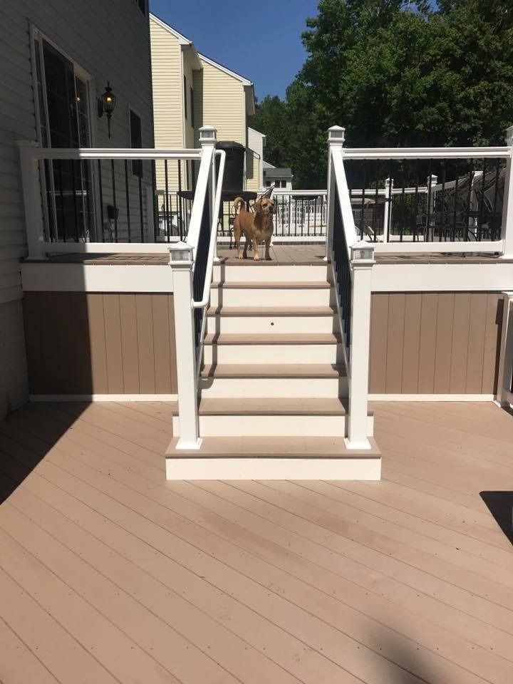White outdoor staircase with railings on a tan deck leading up to a house entrance