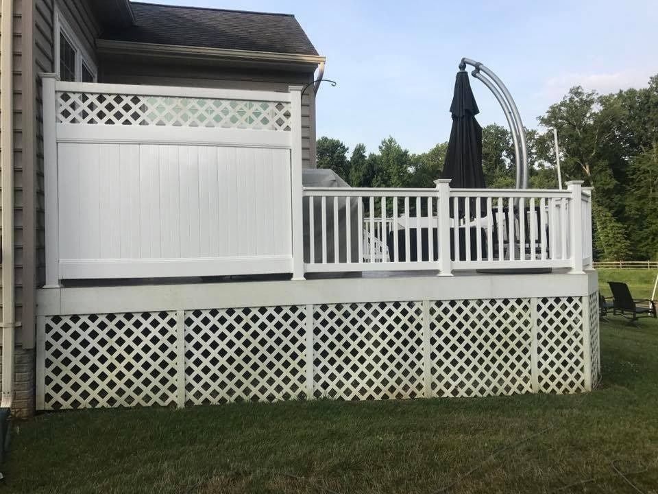 White deck attached to a house with lattice skirting and a closed black patio umbrella.