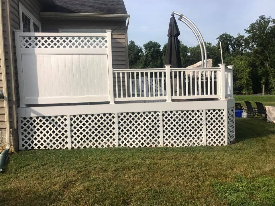 White backyard deck with lattice skirting and railing beside a house, with a closed black patio umbrella.