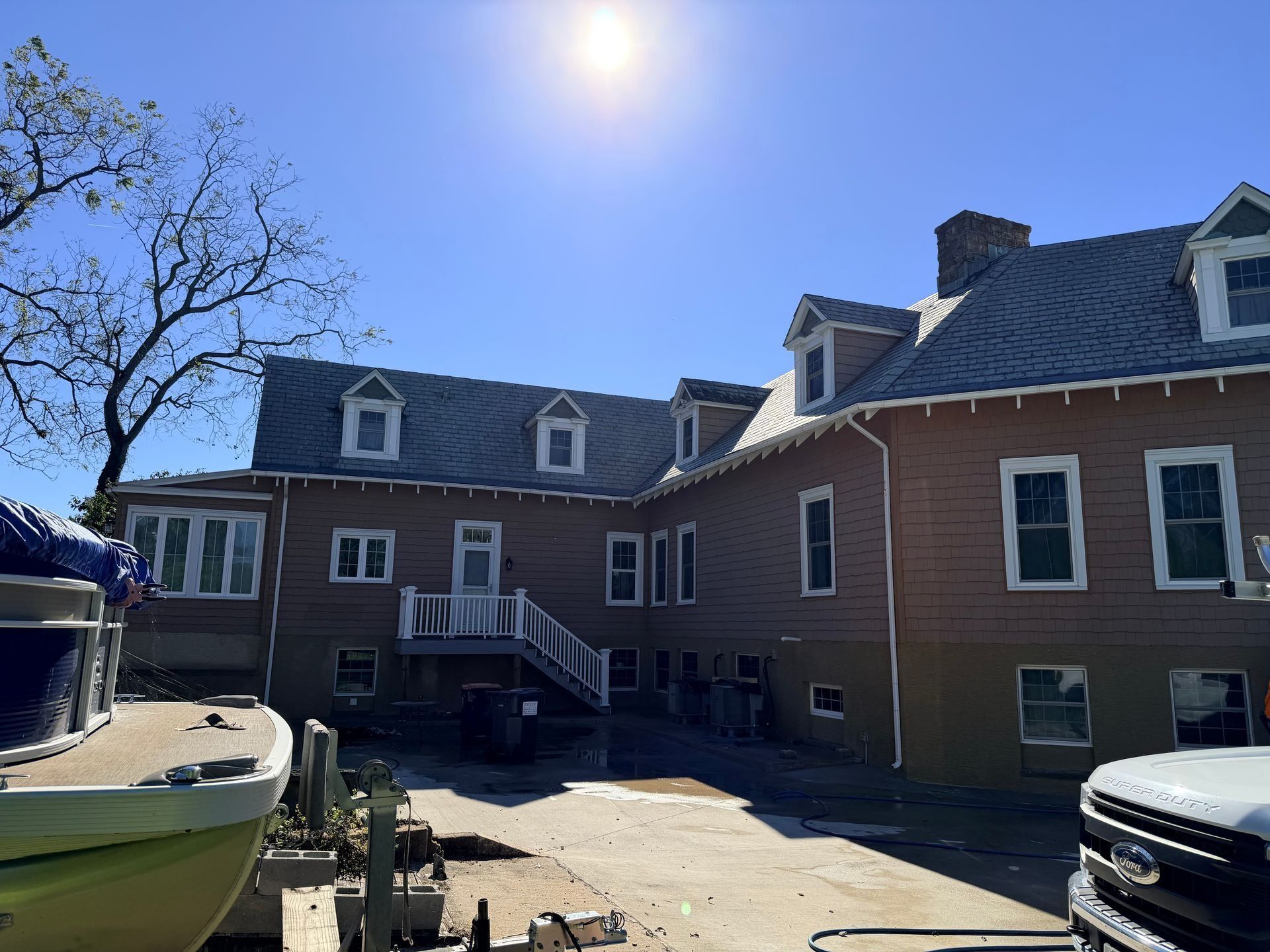 Brick building with dormer windows and sunlit courtyard beside parked boats and cars.