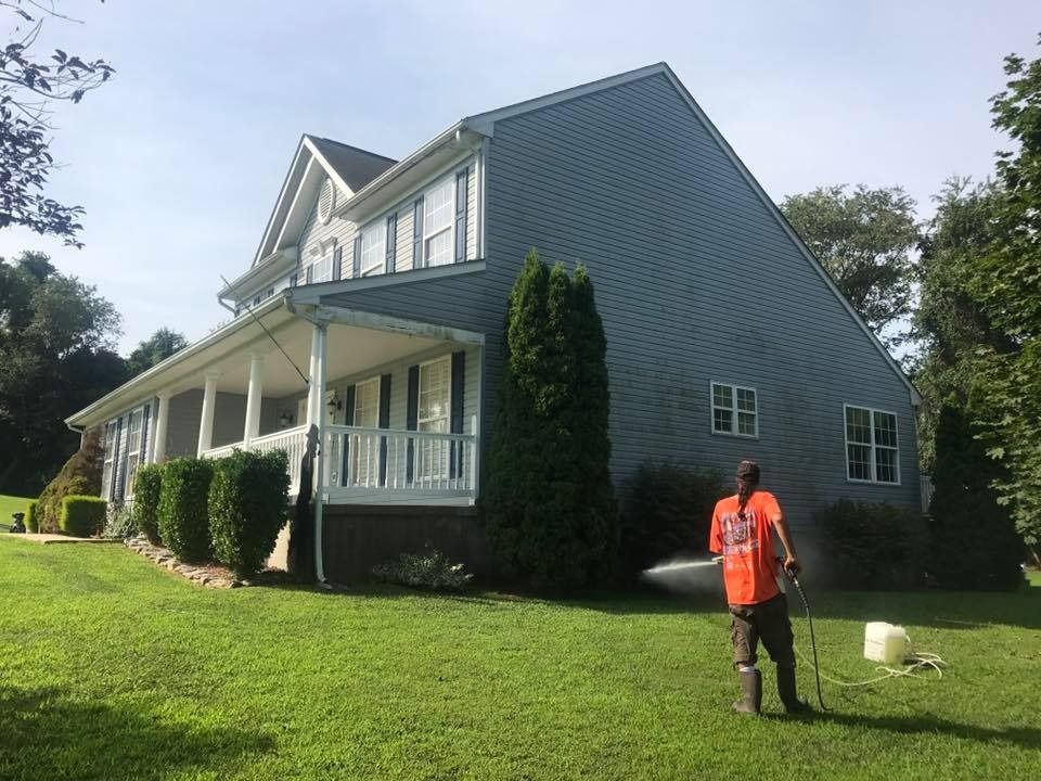 House with white porch and green lawn; person in orange shirt stands holding a leash near a small white dog.