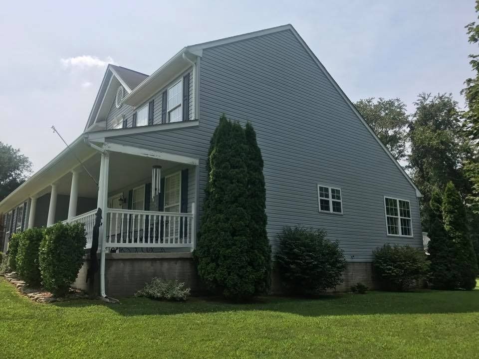 Gray house with white porch and green lawn under a bright sky