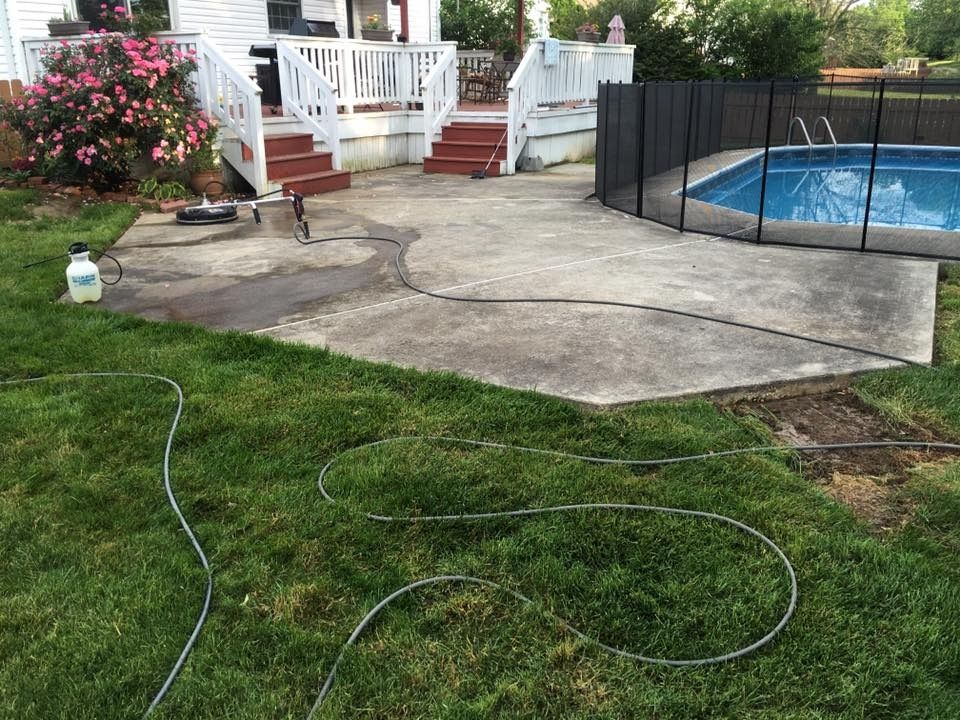 Backyard patio with white deck stairs, flower bushes, and a fenced above-ground pool beside a concrete slab