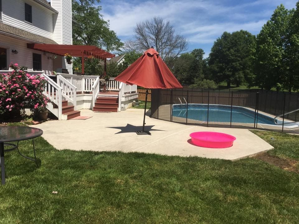 Backyard patio with red umbrella, white deck, and above-ground pool beside green lawn.