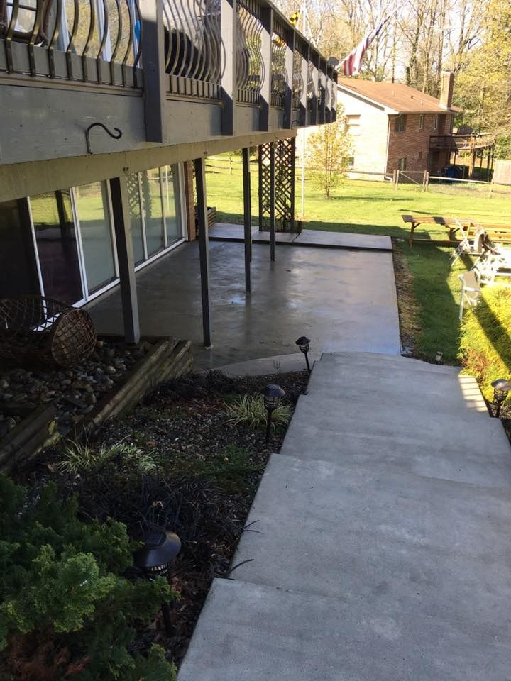 Concrete walkway beside a raised deck, with grass and a small shed in the yard