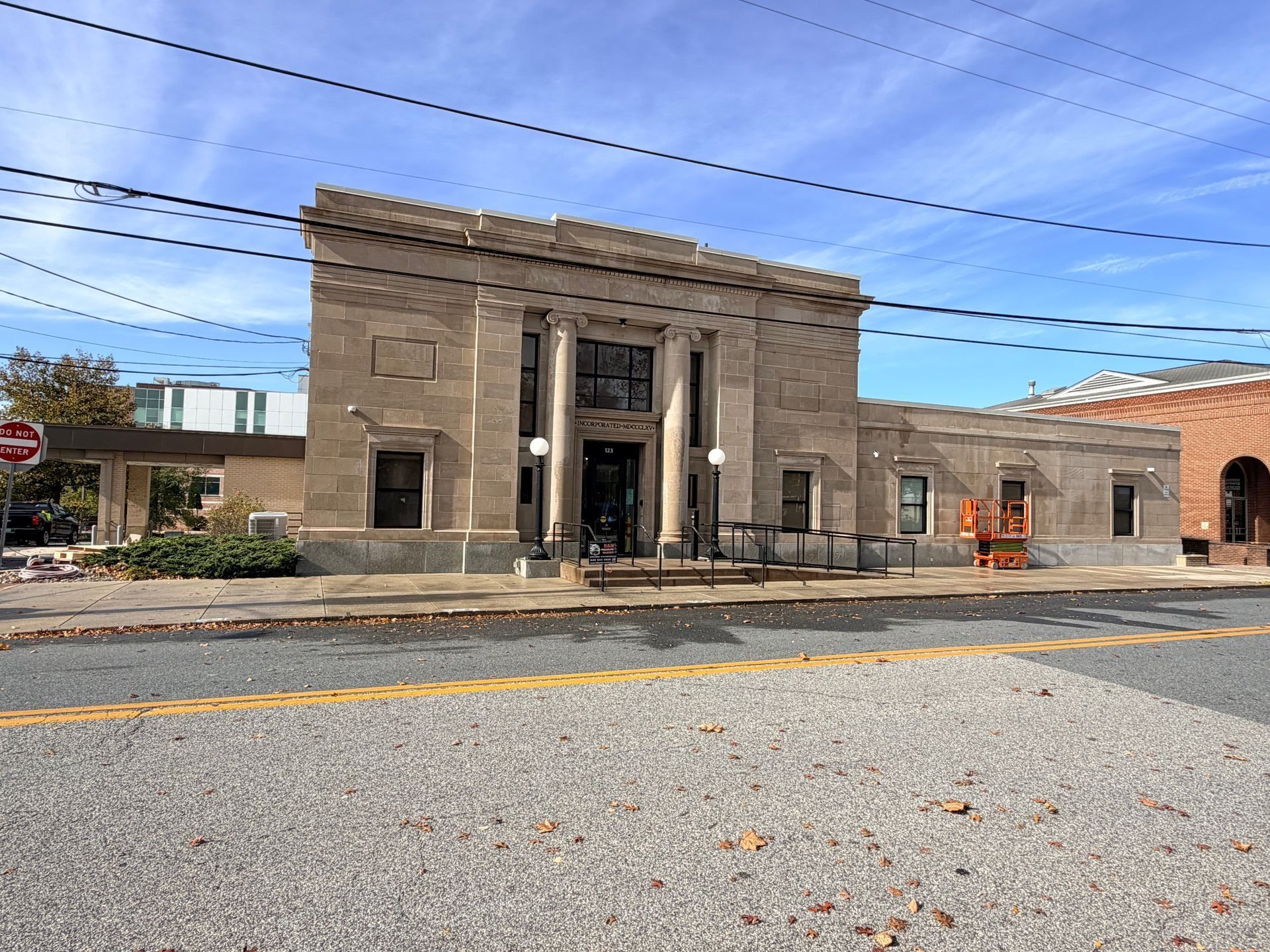 Old stone building with columns and steps beside a paved street under a blue sky.