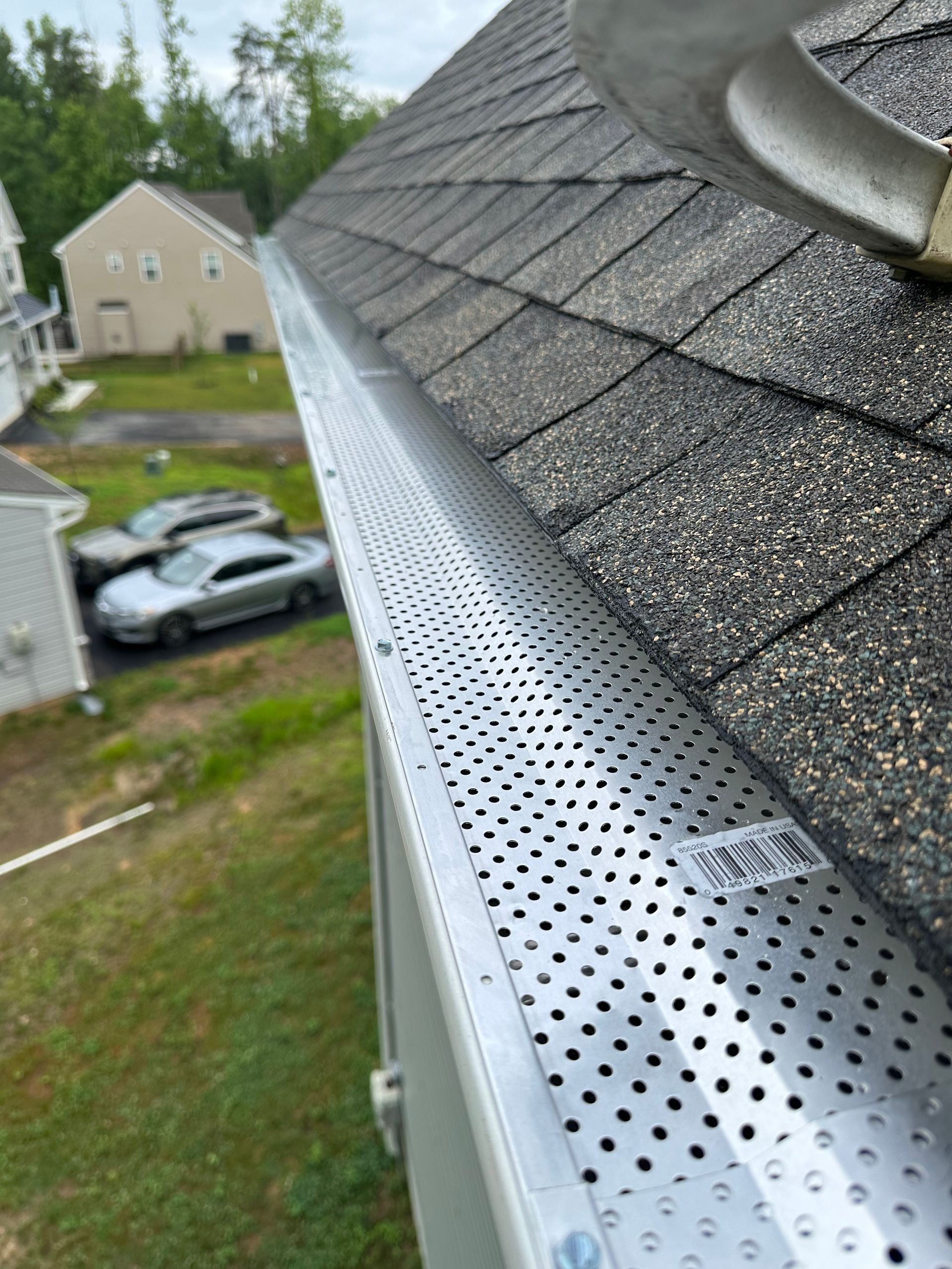 Close-up of a silver gutter with a perforated screen, attached to a gray shingled roof.