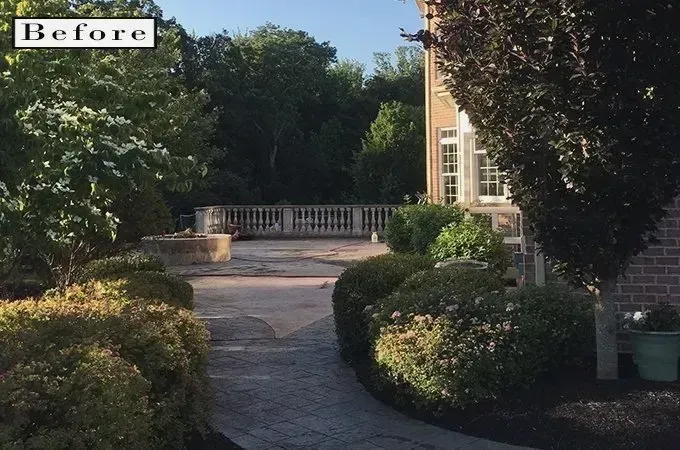 Garden walkway leading to a white bench beside a brick house, with trimmed shrubs and trees.