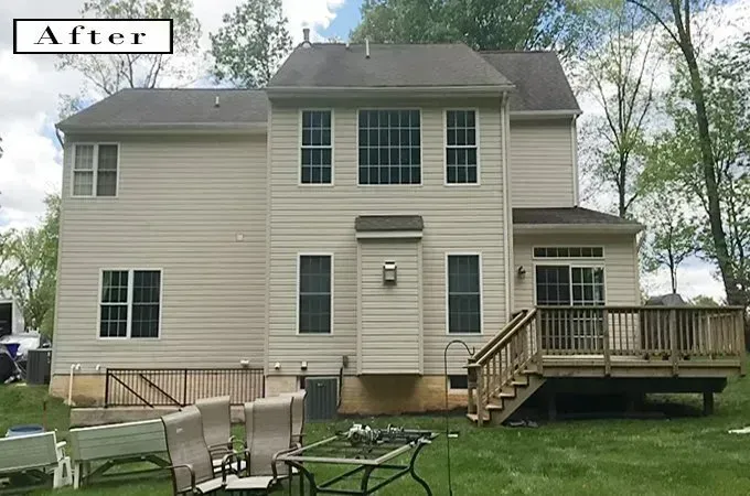 Two-story beige house with a raised wooden deck and patio furniture in a grassy yard