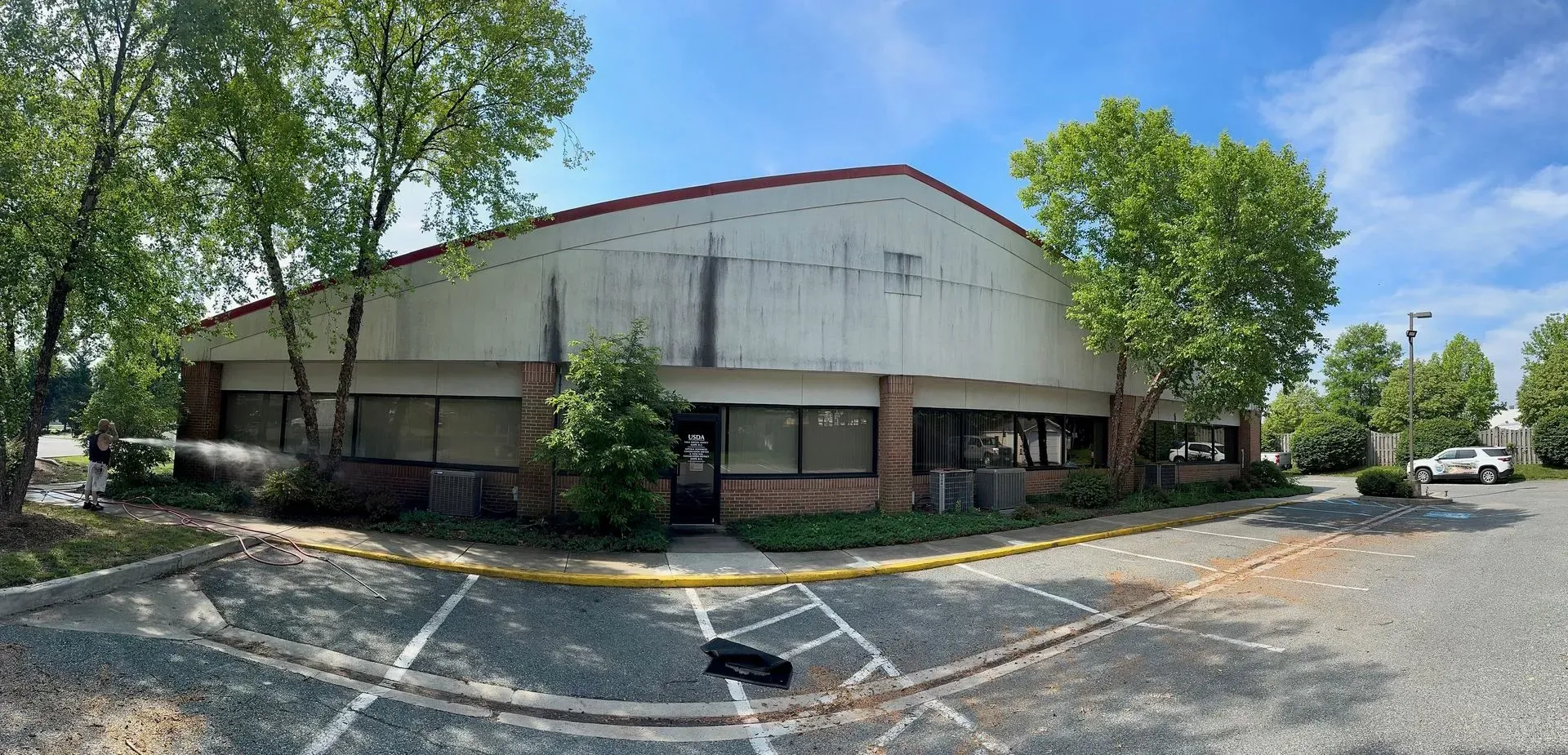 Wide view of a beige commercial building with trees and parking lot under a clear blue sky