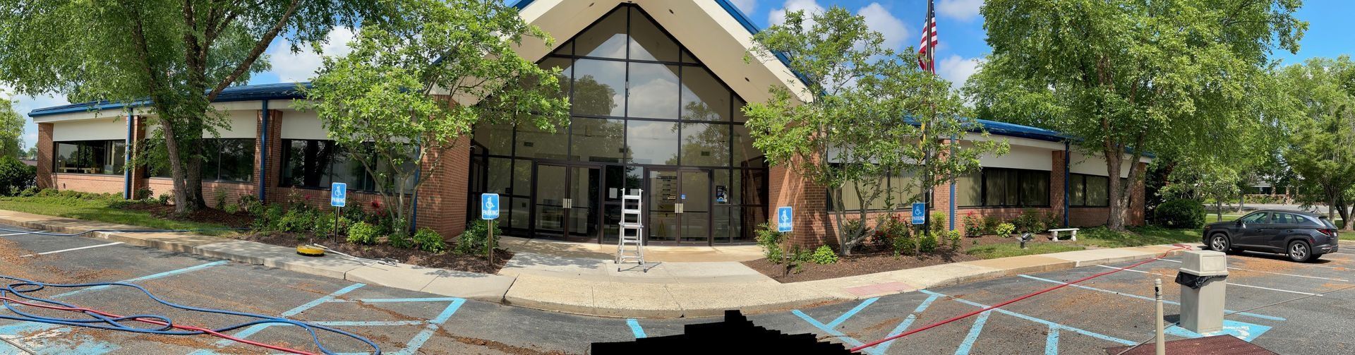 Building exterior with large glass doors, surrounded by trees and a parking lot.