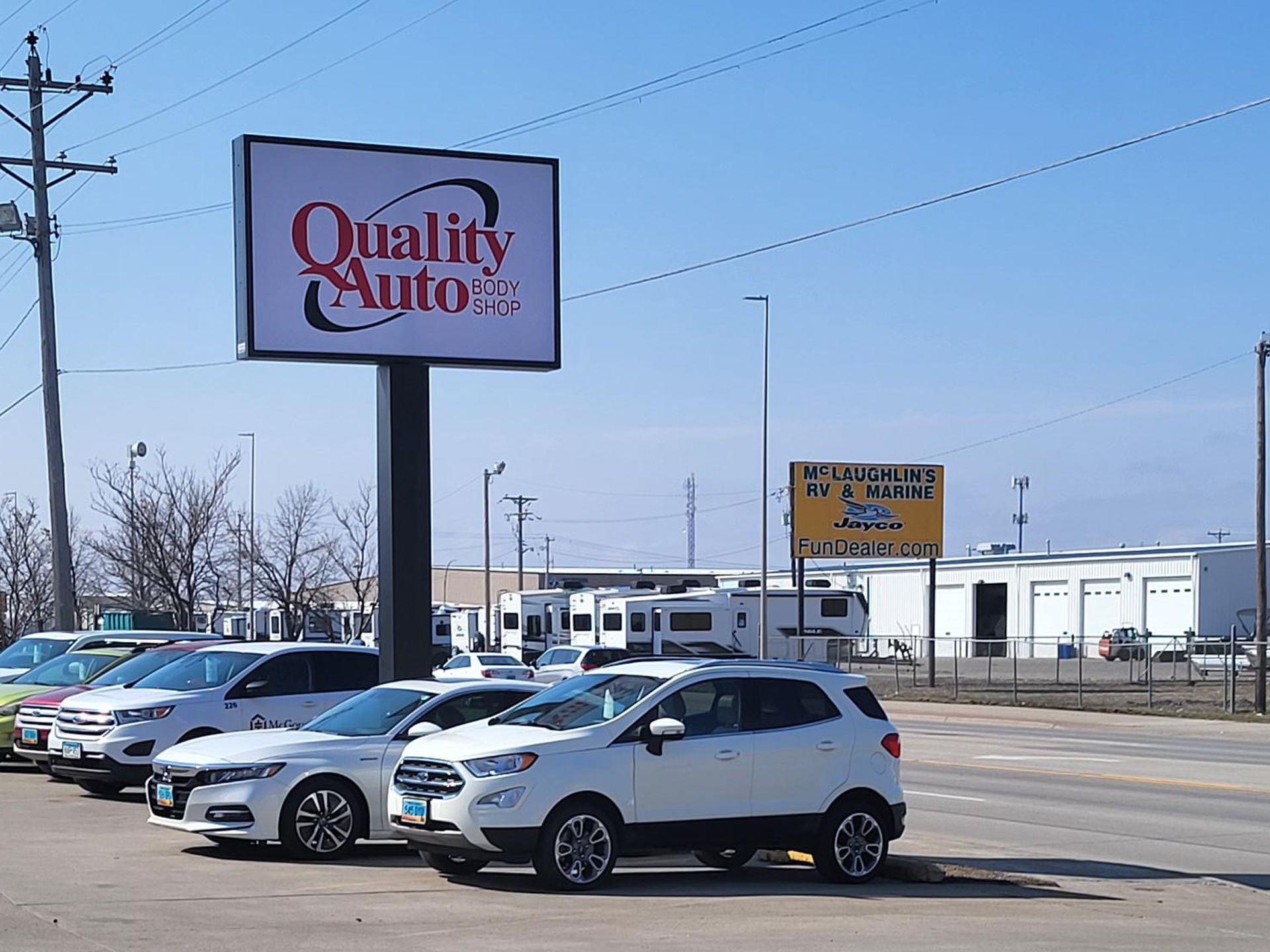 A row of cars are parked in front of a quality auto body shop sign