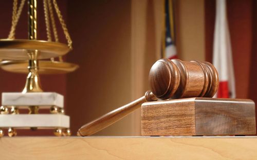 Wooden judge’s gavel on a block beside brass scales of justice in a courtroom setting