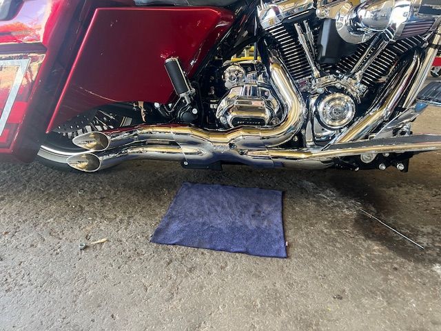 Shiny chrome motorcycle exhaust pipes and engine, a dark blue cloth on the ground.