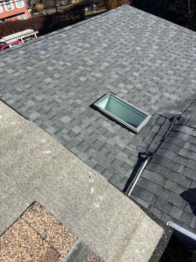 Gray shingle roof with a rectangular skylight, viewed from above, on a sunny day.