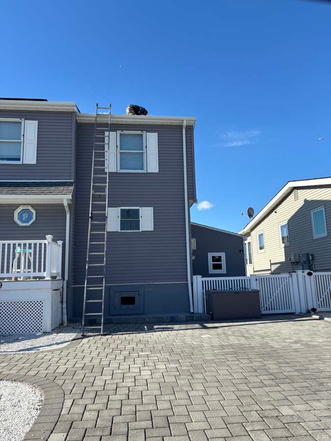 Ladder leaning against a two-story gray house with white trim; clear blue sky above.