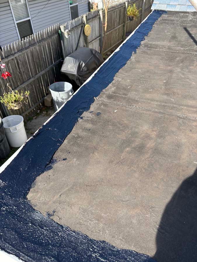 Black asphalt roof edge with dark sealant against a wooden fence and yard with trash cans.