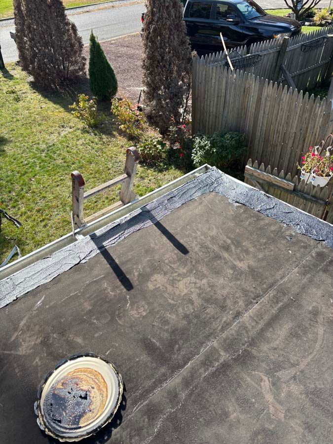 View from a flat roof, showing a ladder, vent, and fence. Green grass and a road are in the background.