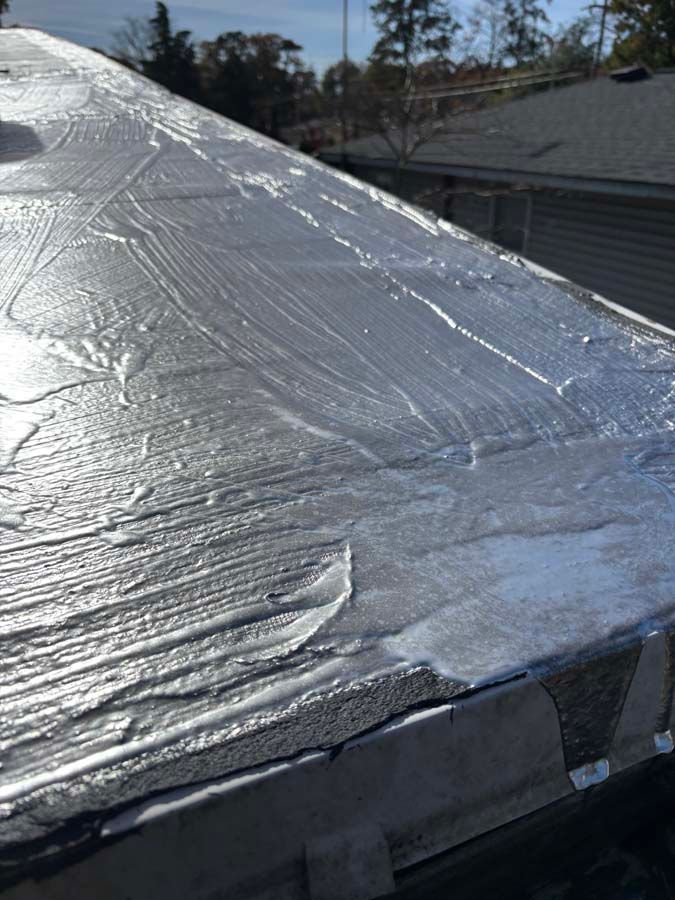 Flat roof with silver sealant applied in uneven streaks.