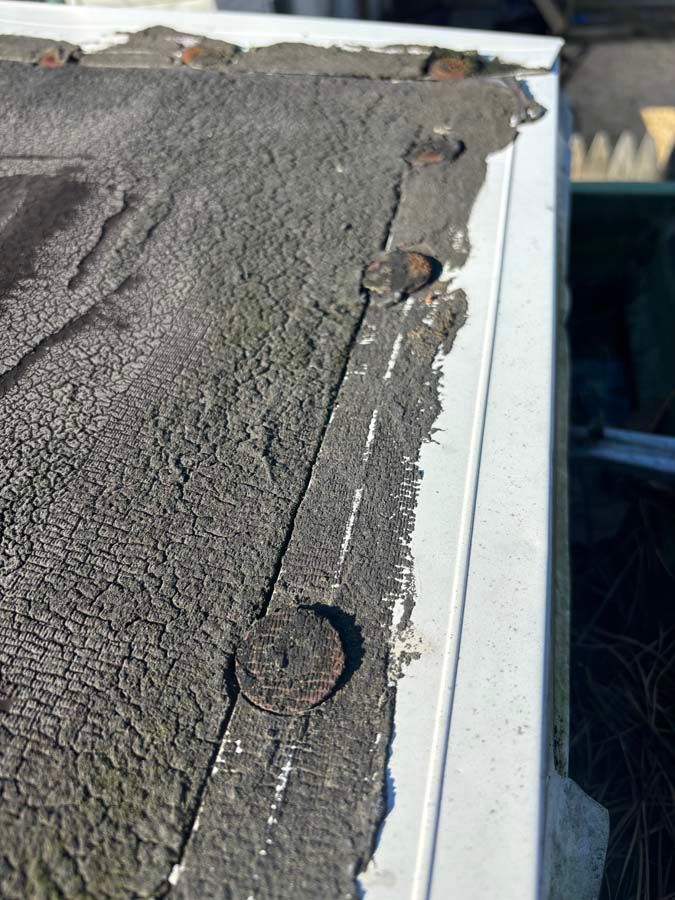 Close-up of a weathered, dark gray roof edge with exposed metal fasteners.