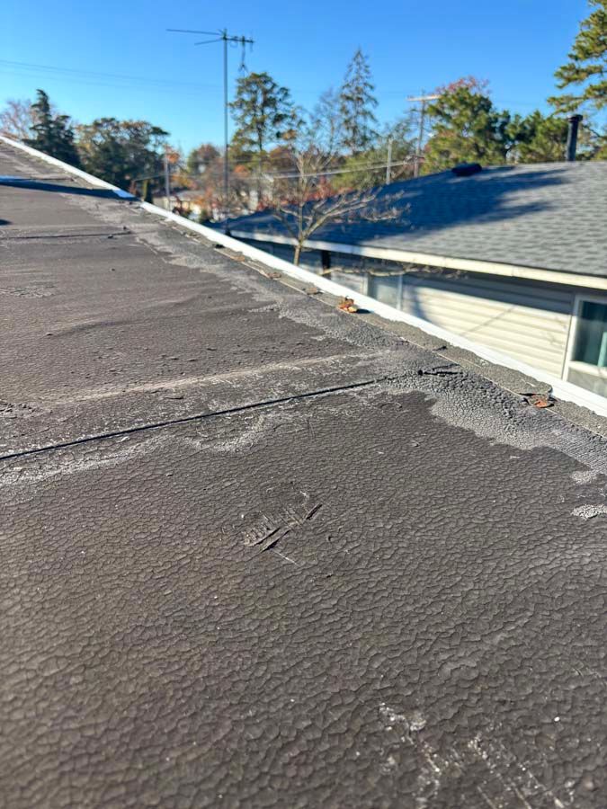 Flat black rooftop with visible seam lines and a gutter on the edge, a sunny day.