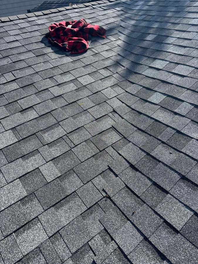 Gray asphalt shingle roof with a red and black plaid garment on it; sunny outdoor setting.