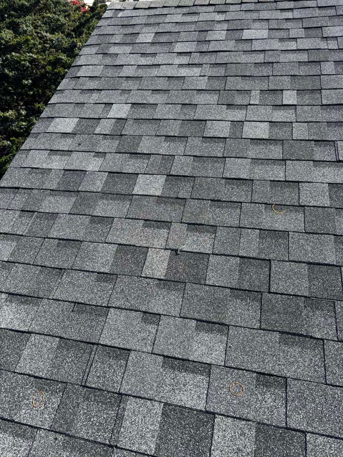 Gray asphalt shingle roof with some missing or damaged shingles; outdoors.