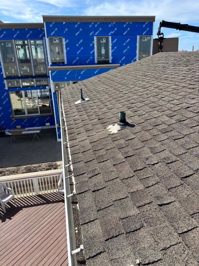 Brown shingle roof with two vents, a gutter, and a partially built blue building in the background.