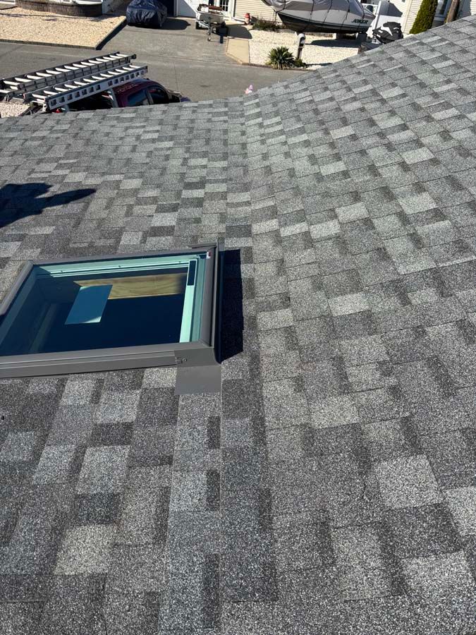 Roof with grey shingles and a rectangular skylight.