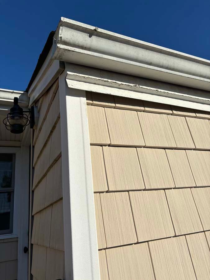 Corner of a house with tan siding and white trim. White gutter along the roof.