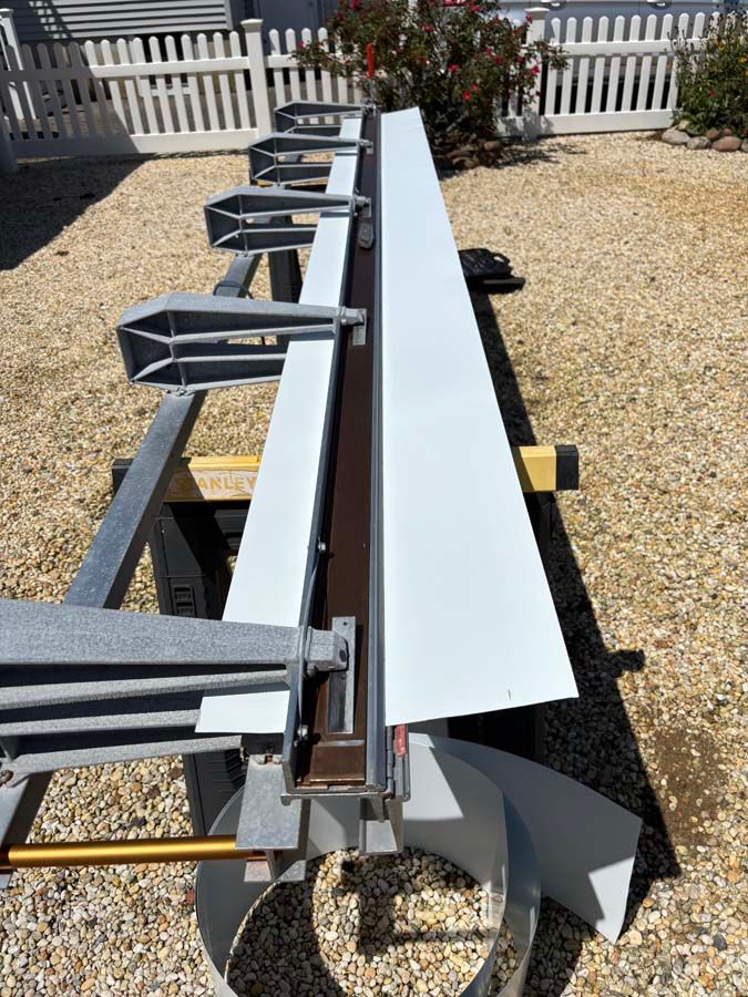 A white metal siding being cut by a siding shear on a gravel surface.