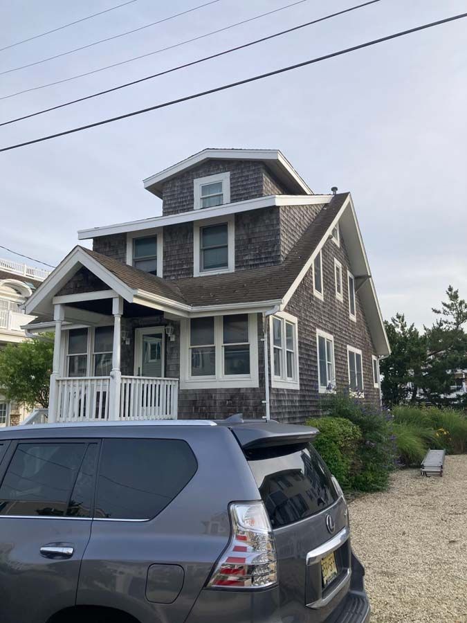 Gray house with white trim, shingle siding, and a covered porch. A gray SUV is parked in front.