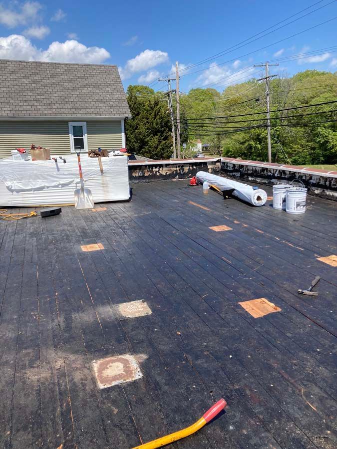 Flat roof being repaired, with materials and tools visible. Bright blue sky overhead.
