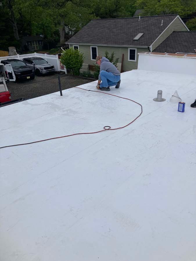 Person on a flat white roof working with a tool, with buildings and cars visible in background.