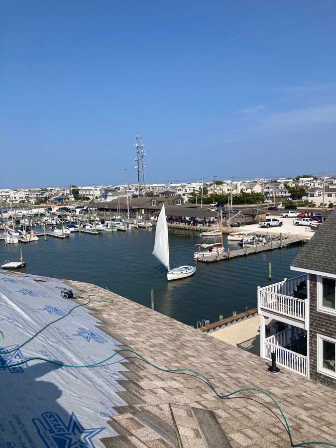 Sailboat on water near a harbor and buildings under a blue sky. Roof in foreground.