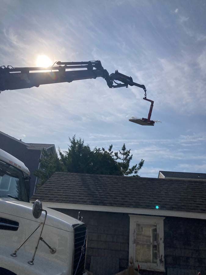 A boom truck with an extended arm lifting an object over a building, sunny sky.