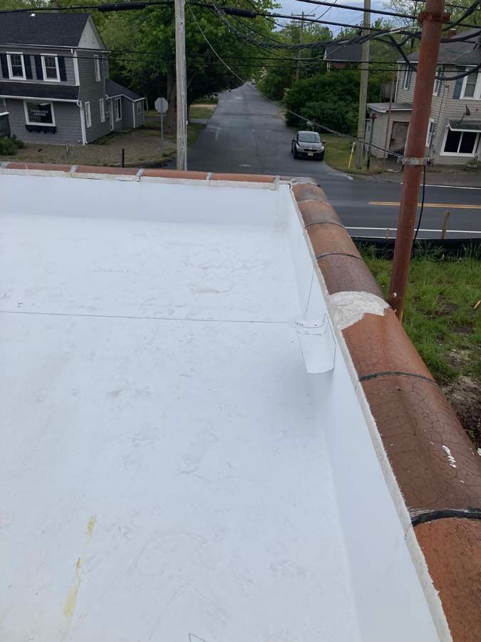 White-coated roof edge with red brick trim, overlooking a road with a parked car and buildings.