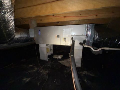 Crawl space under a house with ductwork, insulation, and a black vapor barrier floor.