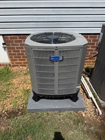 Outdoor central air conditioner unit beside a brick house wall and white siding.