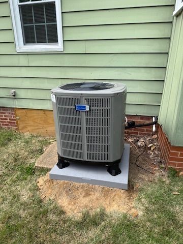 Outdoor air conditioner unit on a concrete pad beside a green house wall