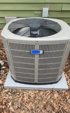 Outdoor air conditioner condenser unit on a concrete pad beside a house, with leaves around it.