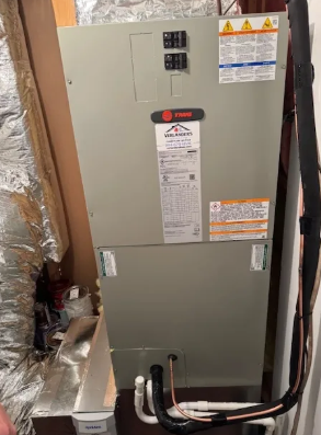 Gray electrical furnace/air handler with wiring in a utility closet, surrounded by insulated ductwork.
