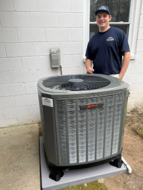 Technician standing beside a large outdoor HVAC unit against a white wall.